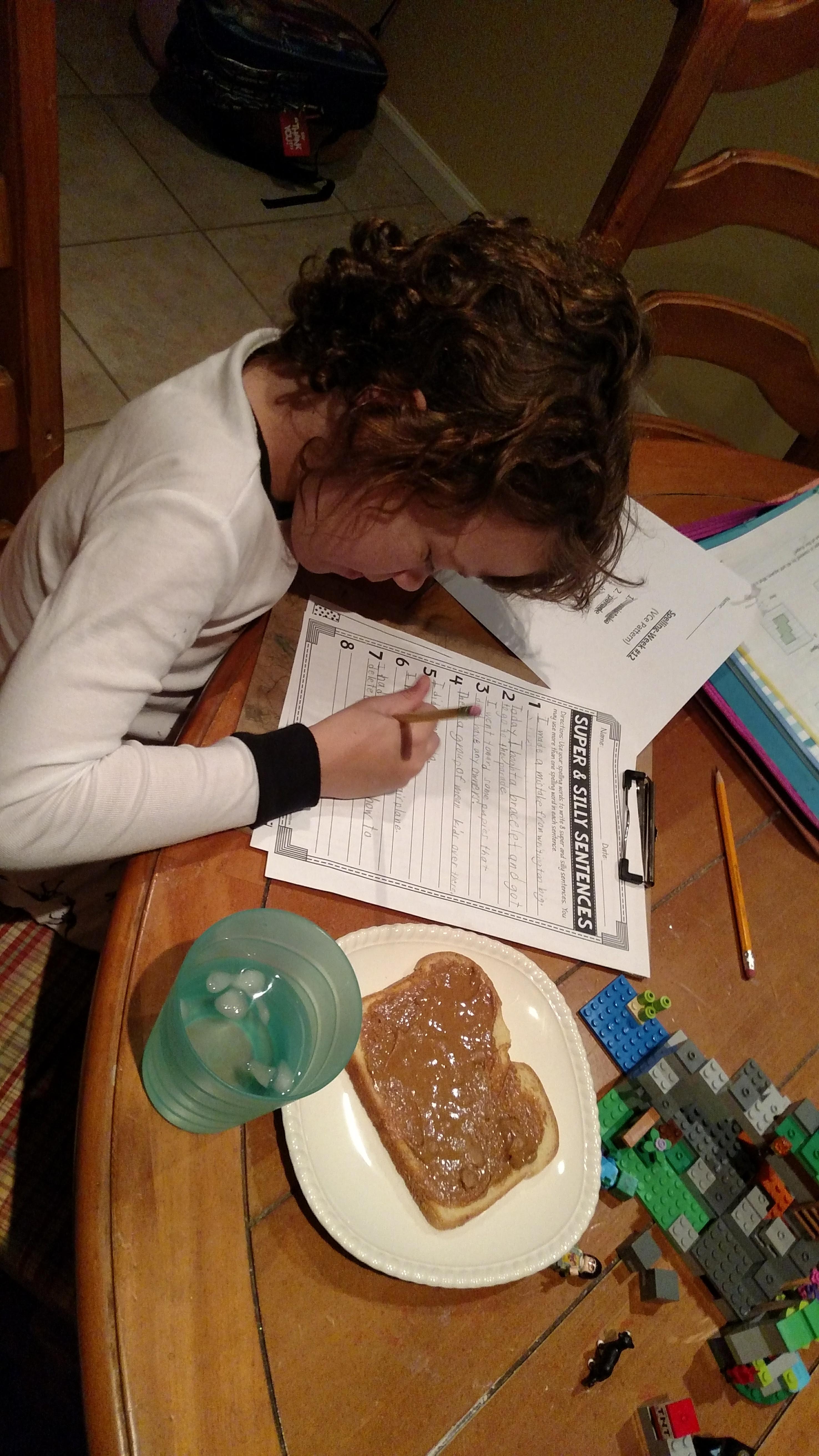 A little girl at the breakfast table doing homework.